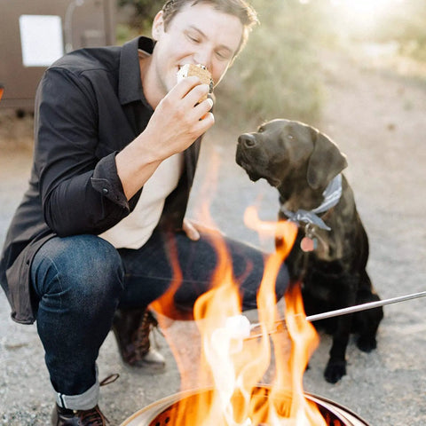 Man roasting marshmallows over Ranger Portable Outdoor Fire Pit With Stand Stainless Steel Firepot, dog watching nearby