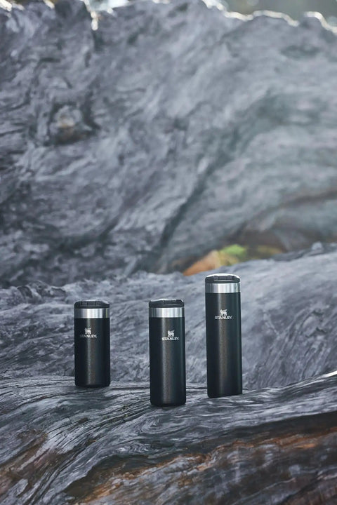Three sizes of black AeroLight 20 Oz Leakproof Stainless Steel Travel Bottle With Locking Lid Vacuum Insulated Double Wall on rock surface.