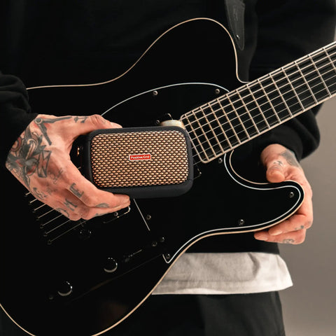 Person holding Ultra Portable 5W Smart Guitar Amp With Bluetooth Speaker Headphone Amp And Mobile App For Electric Acoustic Or Bass Guitars 33 Amps 43 Effects Custom Presets 50,000 ToneCloud Tones next to a guitar