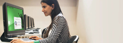 Person using a desktop computer in a row of identical setups in an office environment.