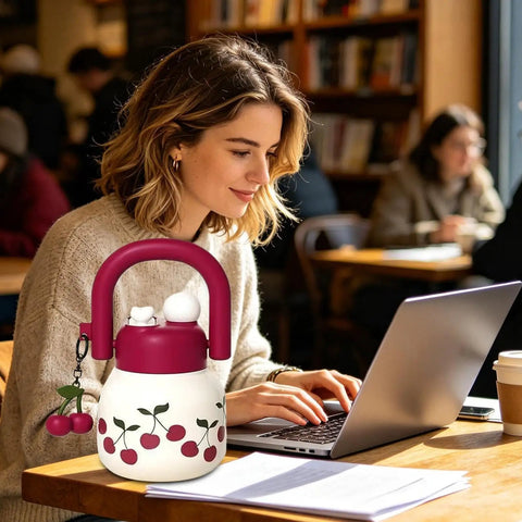 Person using laptop in cafe with a decorative water bottle featuring cherries