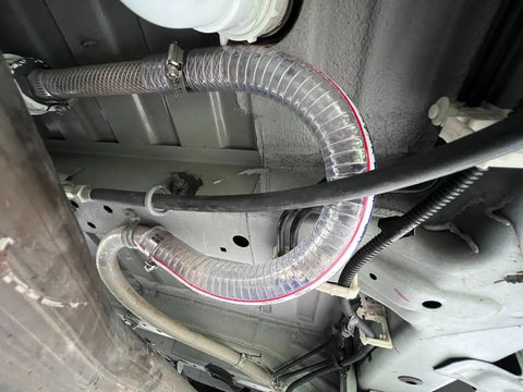 Clear 1 Inch High Pressure Hose With Spiral Steel Wire Reinforcement, 10 Ft Long installed under vehicle for fluid transfer.