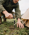 Man hammering black tent stake into grass.