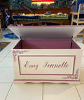 Open wooden toy chest with decorative floral design and personalized name, showing interior supported by soft close hinges for safety.