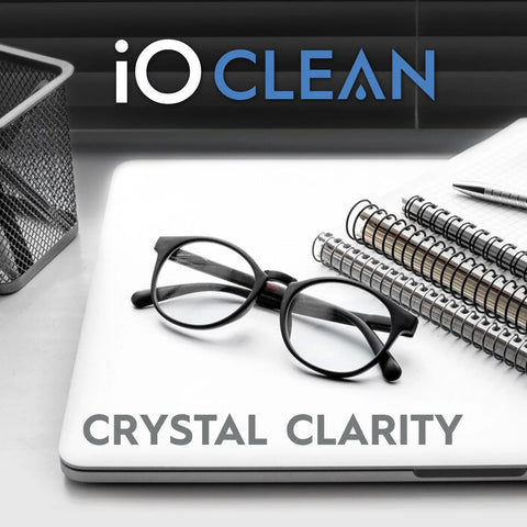 Eyeglass lens cleaner kit, front view: on a laptop with black-framed glasses and notebooks; includes 2 microfiber cloths