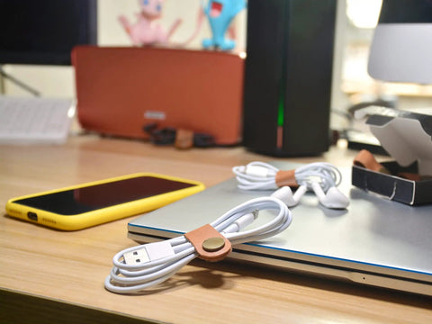Leather Cord Organizer And Cable Keeper Case For Earbuds And Headphones on desk with light brown leather ties and cables