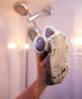 Person applying Shower Door Glass Protectant That Makes Water Bead Off, holding a cloth in a shower with glass doors.