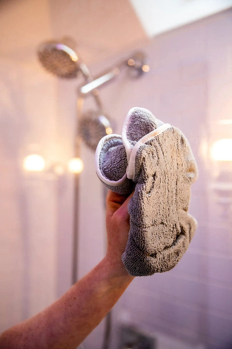 Person applying Shower Door Glass Protectant That Makes Water Bead Off, holding a cloth in a shower with glass doors.
