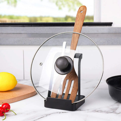Hella Convenient Multi Function Kitchen Utensil And Pot Lid Organizer Pad With Spoon Rest Ladle Holder Catch Mat Drip Tray Washable Heavy Duty Stick Mount Black holding pot lid and spatula on a kitchen counter.