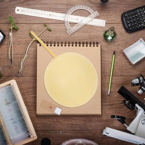 Aerial view of a lab desk with a notebook, ruler, calculator, test tubes, and a microscope on a wooden surface.