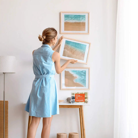 Person hanging picture frame using All In One 276 Piece Picture Hanging Kit With Hangers And Hardware, near light stand and table.