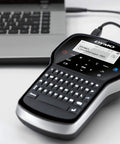 Grab And Go Portable Label Maker With Rechargeable Battery And Qwerty Keyboard next to a laptop, showcasing its compact design.
