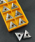 Ten TNMG carbide inserts in a yellow plastic storage case; triangular with center hole for lathe turning.