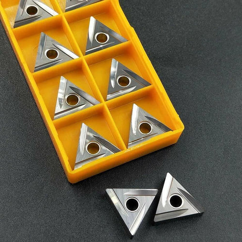 Ten TNMG carbide inserts in a yellow plastic storage case; triangular with center hole for lathe turning.