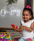 Girl playing near a cool white 'Oh Baby' lit neon sign for wall decor 31.5 by 15.7 inches with dimmable switch.