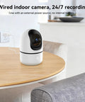 Indoor Security Camera Set With 5G And 2.4G WiFi, 360-Degree Pan Tilt, shown on wooden table, plugged in near wall outlet.
