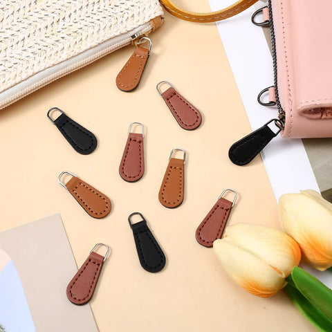 Zipper Pull Tabs Replacement Kit For Luggage Backpacks Jackets Purses And Handbags Grab And Go Easy Clip On PU Leather in black, khaki, and red-brown on a table surrounded by bags.