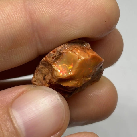 Raw Fiery Jalisco Mexican Fire Opal Stone For Jewelry Making Multicolor Natural Opal Rough Gem With Size 18mm By 16mm By 9mm And Weight 22.60 Ct From Jalisco Mexico Perfect For Beads Cabochons Or Pendant Projects For Unique Jewelry held in fingers