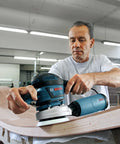 Person using a five-inch soft hook-and-loop sanding pad with eight-hole design on a curved wooden surface.