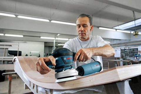 Person using a five-inch soft hook-and-loop sanding pad with eight-hole design on a curved wooden surface.