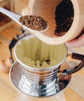 Scooping coffee grounds into 100 Pack 1 To 4 Cup Disposable Basket Coffee Filters For A Smooth Brew Efficient And Convenient 1 Cup Size Eco Friendly Biodegradable Natural Pulp With Wavy Edges And Flat Bottom For Even Filtration in a metal coffee dripper