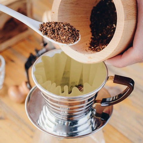 Scooping coffee grounds into 100 Pack 1 To 4 Cup Disposable Basket Coffee Filters For A Smooth Brew Efficient And Convenient 1 Cup Size Eco Friendly Biodegradable Natural Pulp With Wavy Edges And Flat Bottom For Even Filtration in a metal coffee dripper