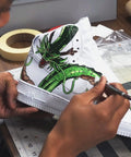 Artist painting dragon design on white shoe using Matte Acrylic Finisher 4 Fl Oz Flexible Clear Coat For Leather Shoes Bags Jackets And Accessories Dope Pro Grade Matte Sealant Varnish For Leather Craft And Restoration Restores Color, Adds Scratch Resistant, Long Lasting Protection No 620.