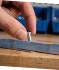 Hand holding a silver aluminum brazier head rivet M5x10 millimeters above metal sheet for leather crafting.