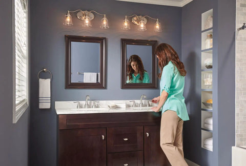 Modern bathroom with dark vanity and mirrors reflecting a woman, emphasizing stylish decor without showing the Hamden Spot Resist Brushed Nickel 24 Inch Single Towel Bar With Easy Install Press And Mark Alignment Fingerprint Resistant Finish Durable Wall Mounted Bathroom Accessory For Coordinating Hamden Collection.