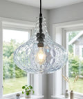 WILON 11" Hammered Glass Pendant Lights Kitchen Island Black hanging above a window, showcasing a clear hammered glass shade.