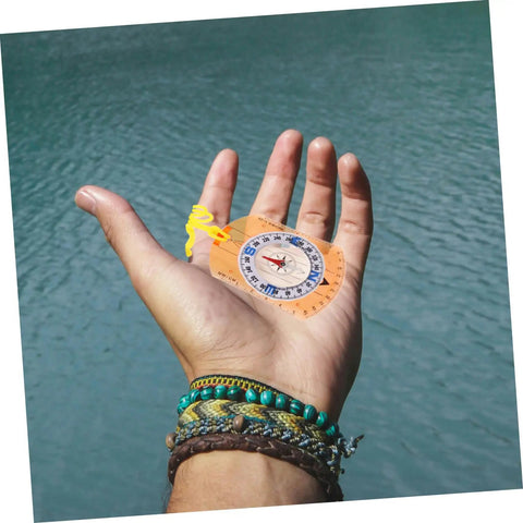 Hand holding Orienteering Compass Pointer All In One Outdoor Navigation Tool, luminous acrylic compact design, by a lake