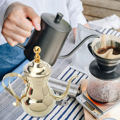 Golden stainless steel Arabic coffee pot and pour over teapot set with infuser next to coffee brewing scene on kitchen table.