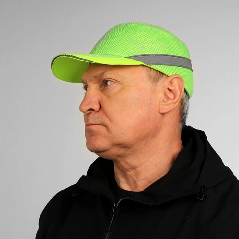 Side view of a man wearing a neon green reflective baseball bump cap hard hat safety helmet with breathable lightweight design.