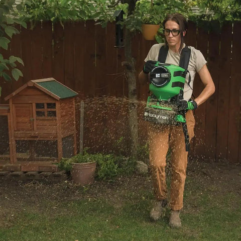 Person using Lithium Ion Chest Spreader With Harness System, Adjustable Feed Rate, 24 Volt Power, 35 Pound Hopper, on lawn