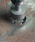 2-inch metal hole saw with carbide-tipped teeth mounted on drill chuck over rusted metal surface