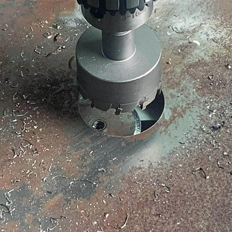2-inch metal hole saw with carbide-tipped teeth mounted on drill chuck over rusted metal surface