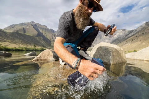 Hiker using Peak Series Collapsible Water Filter Bottle 1L Squeeze Hydration System in a mountain stream.