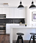 Modern kitchen with white cabinets, black backsplash, and hanging lights over a white island with black stools