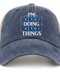 Front view of a purplish blue trucker cap with 'I'm Chuck Doing Chuck Things' text, featuring breathable mesh and curved brim.