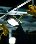 Heavy Duty 100 FT LED String Work Lights with yellow cord hanging in a dimly lit area, showcasing rugged build and usability.