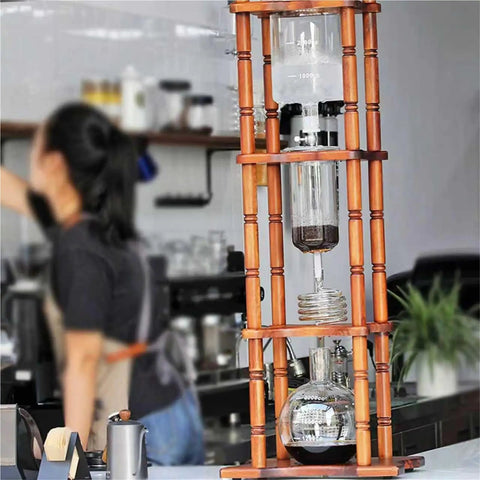 Big Batch Cold Brew Coffee Maker With Adjustable Stainless Steel Dripper And Roomy Borosilicate Glass Carafe displayed on a wooden stand.