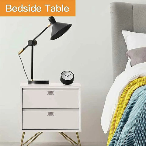 Modern bedside table with drawers, black lamp, and clock next to a bed with colorful bedding.