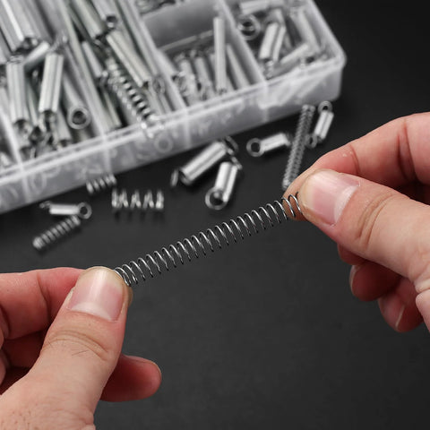 Close-up of a zinc-plated steel coil spring held between fingers; part of a 210-piece spring kit in a plastic organizer