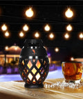 Waterproof Tiki Torch Bluetooth Speaker Two Pack Portable Party Speaker With Flickering LED Lights Perfect For Travel Backyard Parties Poolside And More on table with drink