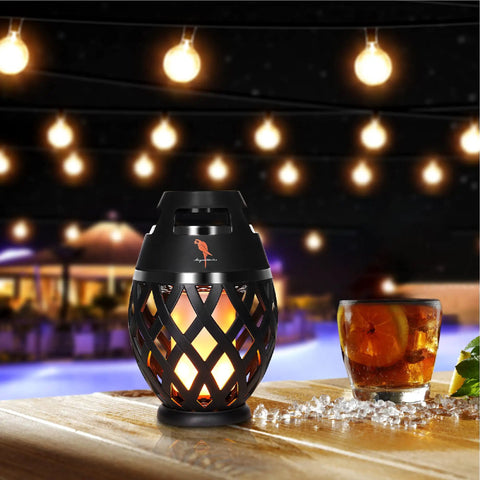 Waterproof Tiki Torch Bluetooth Speaker Two Pack Portable Party Speaker With Flickering LED Lights Perfect For Travel Backyard Parties Poolside And More on table with drink