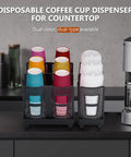 Three Slot Upright Paper Cup And Lid Dispenser For Coffee Stations Keeps 3 Oz To 16 Oz Cups In Check Black Holds Up To 100 Cups And 150 Lids on counter with colorful cups.