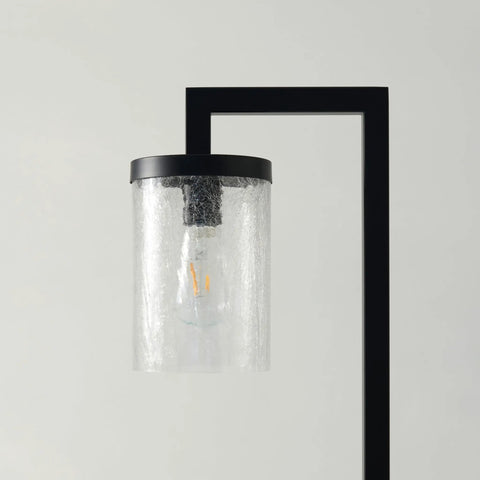 Close-up of a modern cylindrical glass lamp with a black frame and visible bulb inside