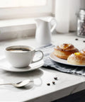 Cup of coffee with pastries on a marble countertop next to a window, morning light illuminating the scene.