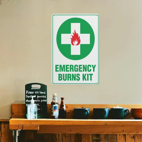 Emergency Burn Care Sign 8x12 Inches Aluminum Warning Plate displayed on a wall above a wooden shelf with items.