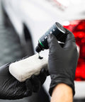 Armour Detail Supply Trim+ exterior plastics restorer being applied from a 50 ml bottle with black-gloved hands onto a cloth.